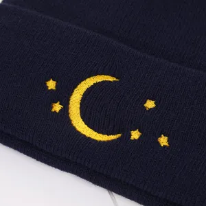 Detailed close-up of navy blue knit beanie featuring yellow moon and star embroidery design.