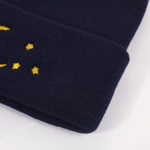 Close-up detail of dark blue winter knit beanie with yellow embroidered stars and crescent moon.