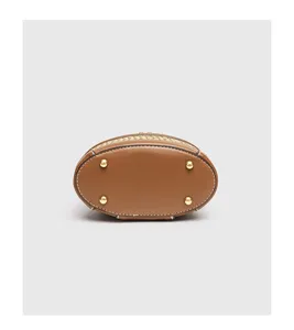 Detailansicht der geflochtenen Strohtasche mit braunem Lederboden und Metallfüßen.