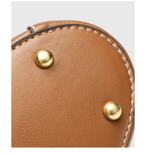 Detailansicht des braunen Ledertaschenbodens mit goldenen Metallfuessen und weissen Naehten.