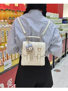 Detailed lifestyle view of white mini backpack with metal hardware and cute plush bear charm.