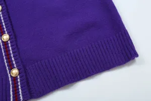 Detail view of the purple knitted cardigan featuring gold buttons and striped placket trim.