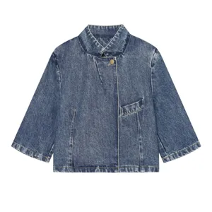 Gedetailleerde close-up van asymmetrische denim jas met opstaande kraag en vintage wassing.