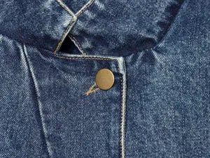 Close-up detail van blauwe denim jas voor dames met opstaande kraag en knoop.