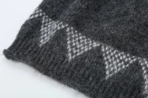 Vista dettagliata di un berretto in maglia grigio scuro con motivo jacquard geometrico bianco.