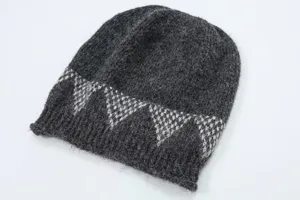Primo piano del berretto in maglia grigio scuro con dettagli geometrici in jacquard bianco.