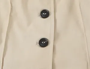 Nahaufnahme des beigen Trenchcoat Stoffes mit eleganten schwarzen Knöpfen und Ziernähten.