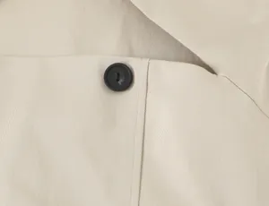 Beige fabric garment detail shot showcasing neat stitching and button close-up style.