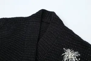 Detailed close-up of a black glitter knit cardigan with elegant pearl sequin brooch.