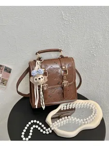 Brown leather mini backpack with embossed cat pattern, vintage schoolbag design with plush charm.