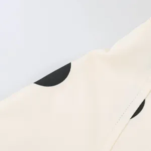 Close-up detail of off-white twill fabric featuring black polka dots and clean stitching.
