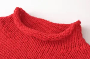 Nahaufnahme des roten asymmetrischen Stehkragen-Strickpullovers mit weicher Wollstruktur.