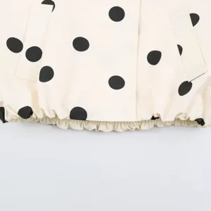 Close up detail of polka dot jacket, cream white fabric with black pattern and elastic hem.