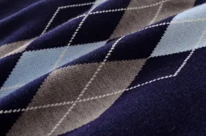 Primer plano de tejido de punto con un patrón de rombos clásico en tonos azul marino, gris y celeste.