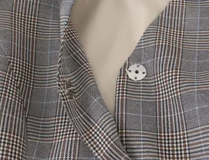 Close-up detail of women's casual plaid blazer showing V-neck design and metal snap button.