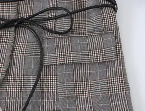 Close-up detail of women's plaid blazer jacket featuring brown pattern and black waist belt.