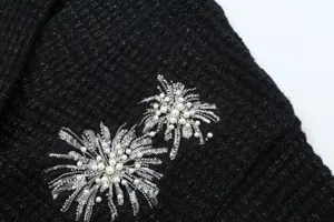 Close-up of black metallic knit fabric featuring detailed sequin and faux pearl embroidery.