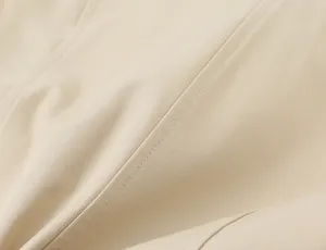 Nahaufnahme der Textur von hochwertigem, beigem Twill-Stoff mit sauberen Nähten für Damenbekleidung.
