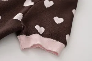 Gros plan sur les détails d'un haut en tricot marron avec des cœurs et des poignets roses.