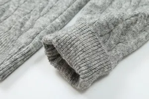 Detailed view of grey knit sweater cuff featuring classic cable knit and ribbed texture.