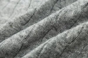 Close-up detail of soft grey knitted fabric texture, featuring fine ribbed knit and draping folds.