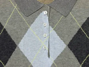 Primer plano detallado de polo de punto gris con patrón argyle clásico y botones blancos.