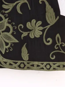 Primer plano de un exquisito bordado floral y de vid verde sobre prenda negra.