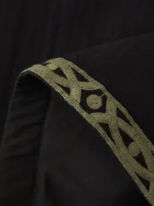 Primer plano detallado del exquisito bordado geometrico en el borde de ropa negro.