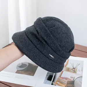 Details of dark grey wool bucket hat, featuring chic pleats and a stylish metal tag accent.