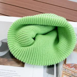 Detailed view of bright green knitted beanie, plain solid color winter warm slouchy cap close up.