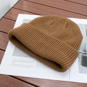 Close-up detail of a cozy brown knitted beanie resting on a styled magazine surface.