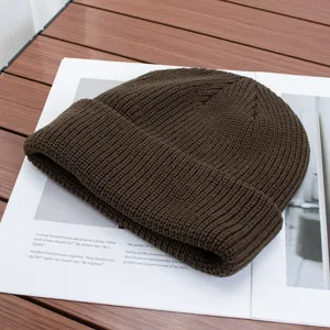 Close-up detail shot of a dark brown knitted beanie hat with ribbed texture and folded cuff.