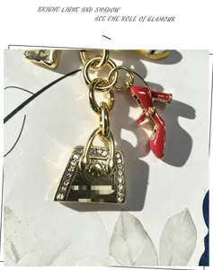 Llavero de metal dorado con zapato de tacón de esmalte rojo y bolso con pedrería elegante.