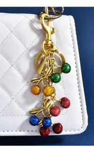Detailed shot of a colorful glitter cherry bag charm with shiny gold alloy leaves and clasp.