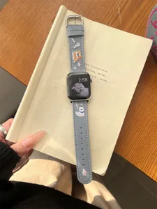 Detailed view of cute embroidered puppy denim watch band on book background, fine craftsmanship.