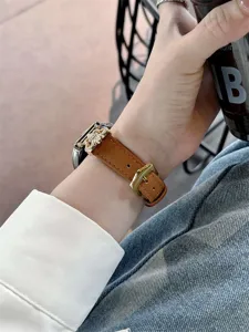 Detailed view of the elegant brown leather smartwatch strap with gold buckle worn on wrist.