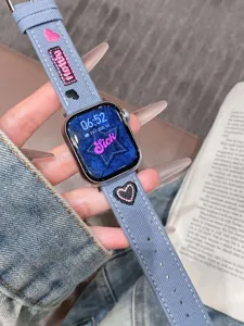 Vue détaillée du bracelet de montre connectée en denim brodé avec des motifs de cœurs.