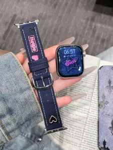 Gros plan détaillé du bracelet de montre en jean avec cœurs et étoiles brodés roses et boucle.