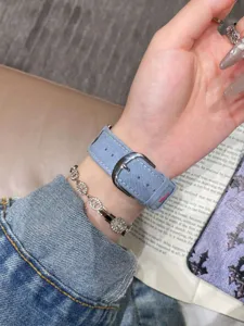 Gros plan détaillé d'un bracelet de montre en jean bleu avec boucle métallique au poignet.