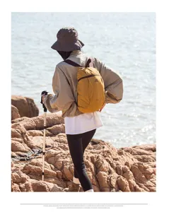 Detailed outdoor lifestyle view of lightweight yellow folding backpack worn by hiker near sea.