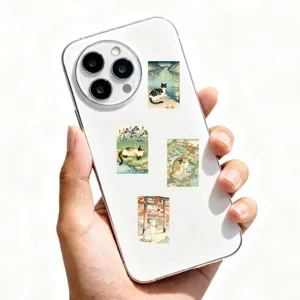 Close-up detail view of retro Japanese ukiyo-e cat stickers pasted on a white smartphone back.