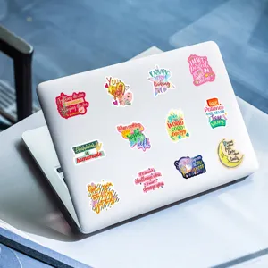 Close up detail of inspiring English text waterproof stickers displayed on a clean white laptop.