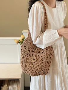 Detailed shot of a stylish brown hollow-out crochet shoulder bag worn with a white dress.