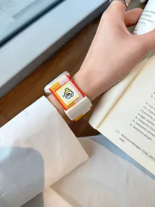 Detail van stijlvol gestreepte Apple Watch band met schattige cartoon badge en magnetische sluiting.