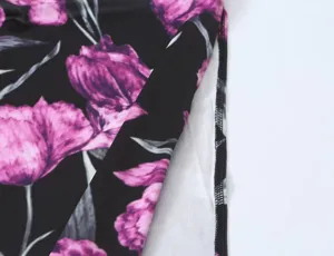 Stofdetail van bloemenprint, close-up opname van paarse bloemen op zwarte gebreide stof.