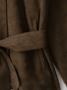 Close-up detail of brown suede jacket with belt and pocket showing fabric texture.