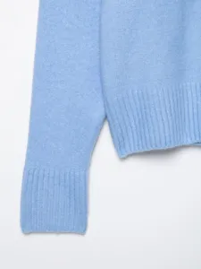 Close-up detail shot showing light blue knitwear sleeve and ribbed hem texture.