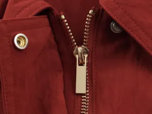 Close-up of stylish metallic zipper and button detail on solid red women's garment collar.