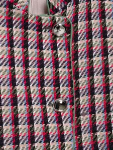 Close-up detail of women's colorful tweed jacket fabric texture with green trim and metallic buttons.