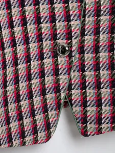 Detailed close-up of colorful tweed fabric, metallic button, and green trim on stylish blazer.
